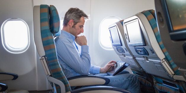 Businessman using digital tablet on airplane.