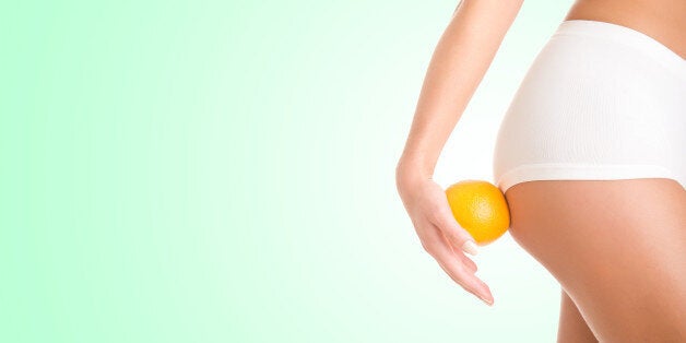 Woman holding an orange against her thighs, isolated in green