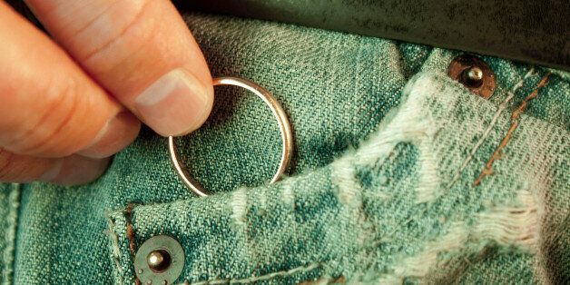 Closeup of a man?s hand put in or taking out a wedding ring in the worn jeans pocket. Concept of infidelity or asking in marriage.