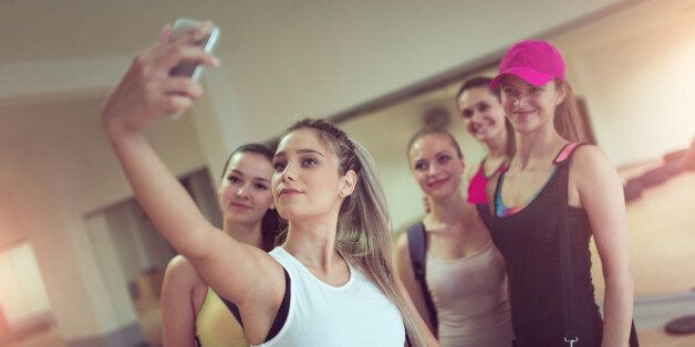 Group of young smiling athletic females how Taking Selfie in Gym after Exercise.