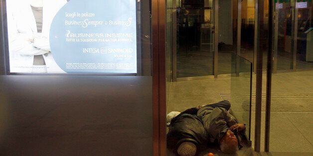 A homeless man sleeps inside the withdrawal area of a bank in downtown Milan February 9, 2012. Sub-freezing winter weather temperatures continued to hit Europe. REUTERS/Stefano Rellandini (ITALY - Tags: ENVIRONMENT SOCIETY POVERTY)