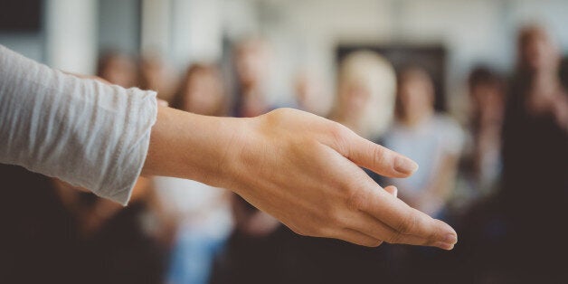 Close up of female hand against defocused group of students. Unrecognizable people.