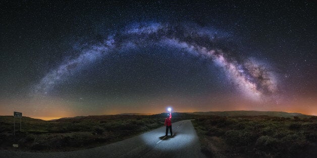 A young man on a road watching the Milky Way and lightning the road with a flash. Taken in A Veiga, Orense.