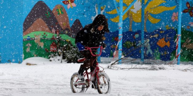 A stranded refugee boy rides his bicycle through a snowstorm at a refugee camp north of Athens January 10, 2017.REUTERS/Yannis Behrakis