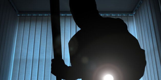 Burglar or intruder inside of a house or office with flashlight and baseball bat