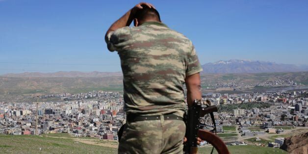 TOPSHOT - A Turkish soldier gestures while standing on the hill overlooking damaged buildings following heavy fighting between government troops and Kurdish fighters in the Kurdish town of Cizre in southeastern Turkey, which lies near the border with Syria and Iraq, on March 2, 2016. Thousands in Turkey's Kurdish-majority town of Cizre started returning to their homes on March 2 after authorities partially lifted a curfew in place since December for a controversial military operation to root out separatist rebels. / AFP / YASIN AKGUL (Photo credit should read YASIN AKGUL/AFP/Getty Images)