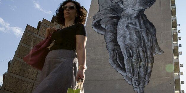A woman walks past a mural of praying hands in Athens, Greece June 25, 2015. Greece's ruling Syriza party dismissed reform demands from the country's international creditors as