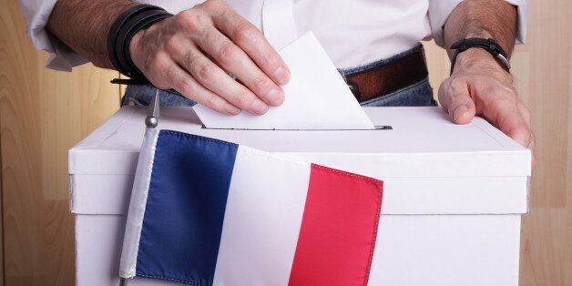 A man inserting a ballot to a ballot box. French flag in front of it.