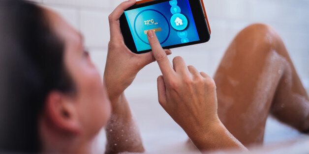 Woman using mobile app in bathtube checking temperature of her house.