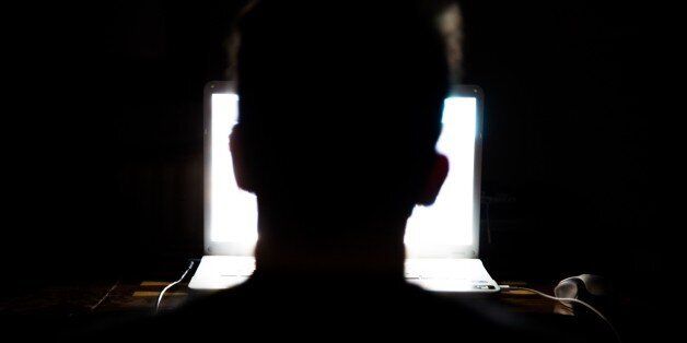 Man sitting in front of a laptop computer in the dark night with the only light of the screen, connected to internet everytime, addiction to the new technologies.