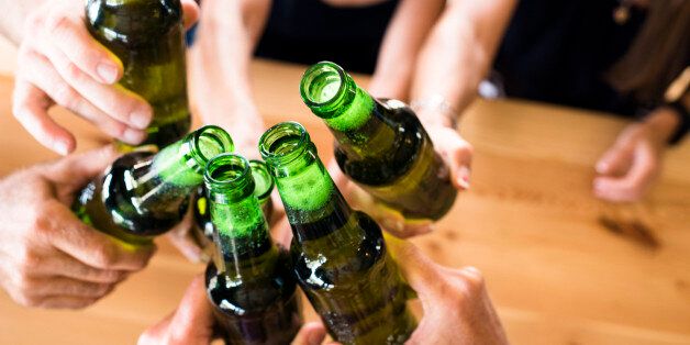 Group of friends seated at a table toasting generic bottles at an indoor brewery.