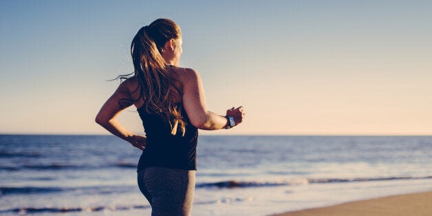 Long blond haired woman jogging at beach with smartwatch into sunlight.