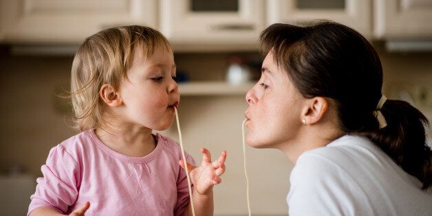 Mother and her little child sucking together spaghetti noodles.