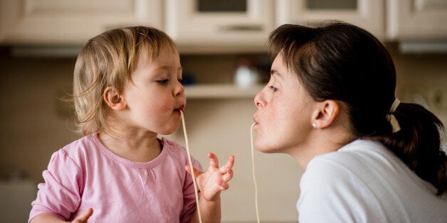 Mother and her little child sucking together spaghetti noodles.