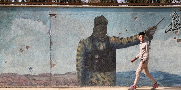 MOSUL, IRAQ - JANUARY 30: An Iraqi boy walks in front of a mural painting, drawn by Daesh Terrorists, after the city has been retaken from Daesh terrorists in Mosul, Iraq on January 30, 2017. (Photo by Yunus Keles/Anadolu Agency/Getty Images)