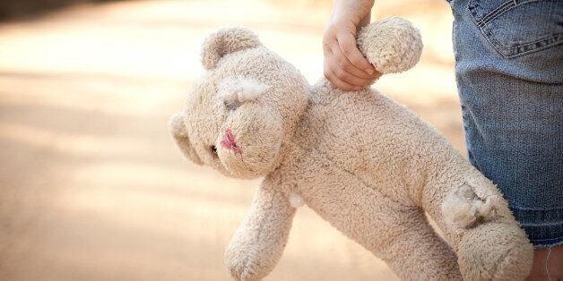 Color stock photo of a little runaway girl holding an old teddy bear at the side of a dirt road in the rural country.