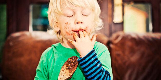 Little boy licking chocolate off his fingers and wooden spoon while making cakes.