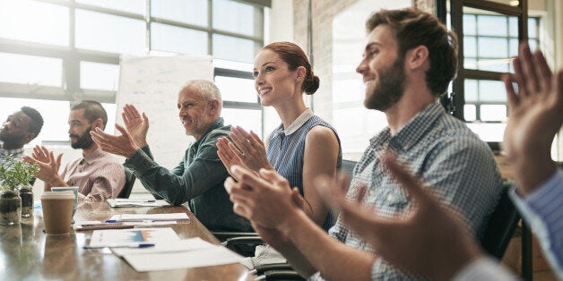 Shot of a team of businesspeople clapping hands while having a meeting in an office