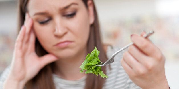 Displeased young woman eating green leaf lettuce. Shallow depth of field, focus on foreground