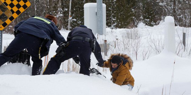 A man who told police that he was from Mauritania is helped up a hill and taken into custody by Royal Canadian Mounted Police (RCMP) officers after walking across the U.S.-Canada border into Hemmingford, Quebec, Canada February 13, 2017. Picture taken February 13, 2017. REUTERS/Christinne Muschi