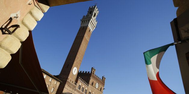 The Italian national flag flies in an entrance to the Piazza del Campo with the Torre del Mangia in the...