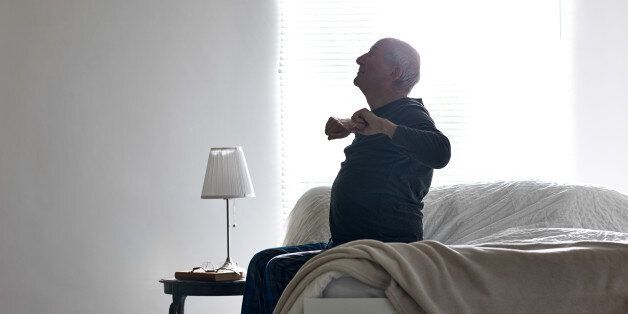 Senior man sitting on bed stretching his arms - Morning exercises