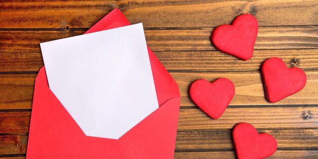 Red envelope with empty paper and cookie heart on wooden table