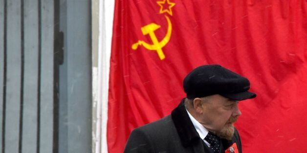 An impersonator of Soviet state founder Vladimir Lenin walks past a hammer-and-sickle red flag in central Moscow on February 14, 2017. / AFP / Vasily MAXIMOV (Photo credit should read VASILY MAXIMOV/AFP/Getty Images)
