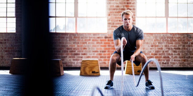 Athletic young adult caucasian man doing battle ropes exercise during a gym training at the gym