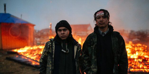 CANNON BALL, ND - FEBRUARY 22: Chanse Zavalla, 22, left, and O'Shea Spencer, 20, right, stand in front of the remains of a hogan structure. Campers set structures on fire in preparation of the Army Corp's 2pm deadline to leave the Oceti Sakowin protest camp on February 22, 2017 in Cannon Ball, North Dakota. Activists and protesters have occupied the Standing Rock Sioux reservation for months in opposition to the completion of the Dakota Access Pipeline. (Photo by Stephen Yang/Getty Images)