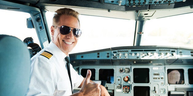 Rear view of confident male pilot showing his thumb up and smiling while sitting in cockpit