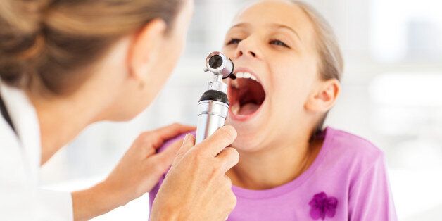 Cropped image of female doctor examining girl's throat with otoscope in clinic. Horizontal shot.