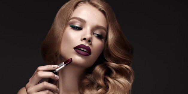 Beautiful blonde in a Hollywood manner with curls, dark lips, lipstick in hand. Beauty face and hair. Picture taken in the studio