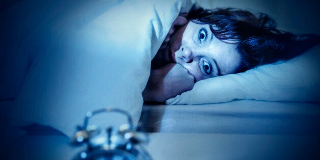 young woman in bed with alarm clock and eyes opened suffering insomnia and sleep disorder thinking about his problem on dark studio lighting in sleeping and nightmare issues