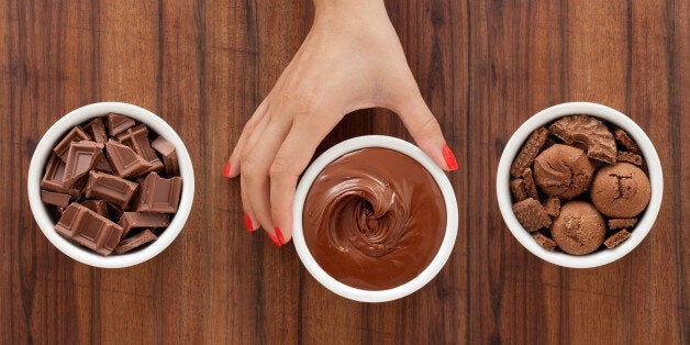 Three bowls with varieties of chocolate foods and woman's hand holding the middle one