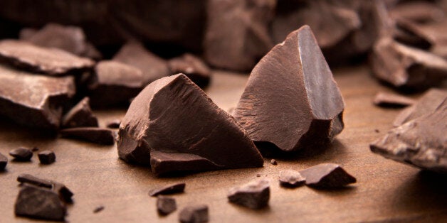 Pieces of dark chocolate spread out on a wooden background.