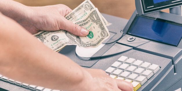 Cashier holdnig banknotes and using cash register at shop