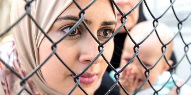 Middle eastern women posing looking looking through a fence very sad one is holding a crying baby
