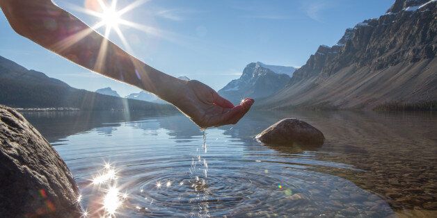 Human hand cupped to catch the fresh water from the lake, sunlight from sunset passing through the transparence of the water.