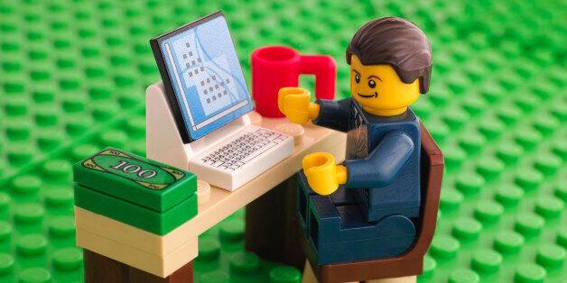 Tambov, Russian Federation - March 24, 2015: Lego businessman sits at his working table with computer, money and cup on Lego green baseplate background. Studio shot.