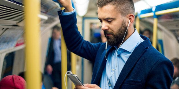 Serious businessman with headphones travelling to work. Standing inside underground wagon, holding handhandle.