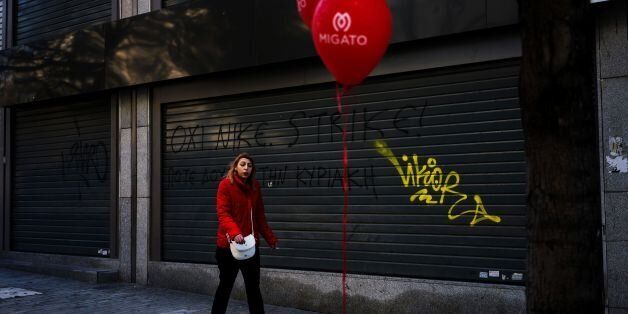 A woman walks in front of a closed shop with a graffiti tag reading 'strike' in the center of Athens in January 8, 2017. / AFP / Angelos Tzortzinis (Photo credit should read ANGELOS TZORTZINIS/AFP/Getty Images)