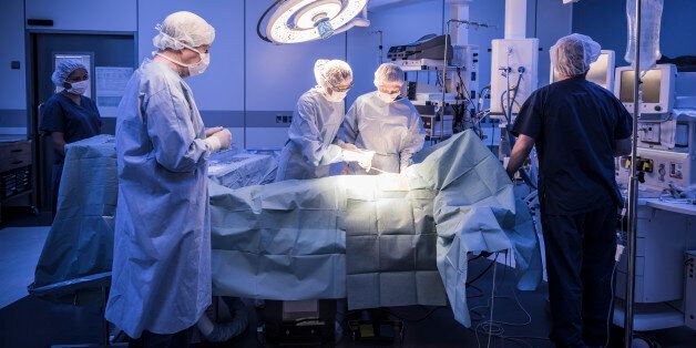 Four doctors in hospital operating room with patient lying on operating table. Surgical lights shining on medical team performing operation on patient