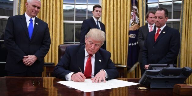 US President Donald Trump signs an executive order as Vice President Mike Pence and Chief of Staff Reince Priebus look on at the White House in Washington, DC on January 20, 2017. / AFP / JIM WATSON (Photo credit should read JIM WATSON/AFP/Getty Images)