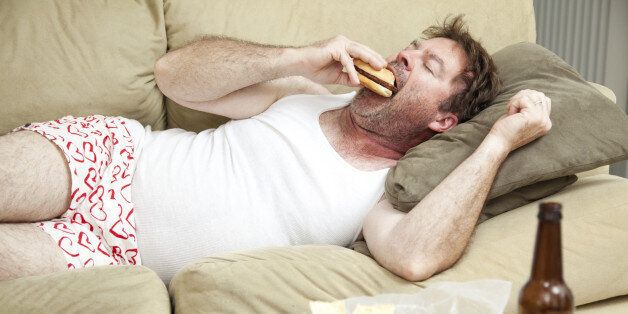 Unemployed middle aged man at home on the couch in his underwear, eating a hamburger, with a marijuana joing in the ashtray and beer bottles lying around.
