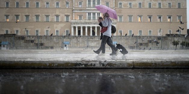 Tourists walk under the rain in front of the Greek Parliament in Athens on November 6, 2013. AFP PHOTO / ARIS MESSINIS (Photo credit should read ARIS MESSINIS/AFP/Getty Images)