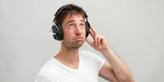 Young man with casual white T-Shirt and heandphones making disapproving, bored face. Grey studio background.