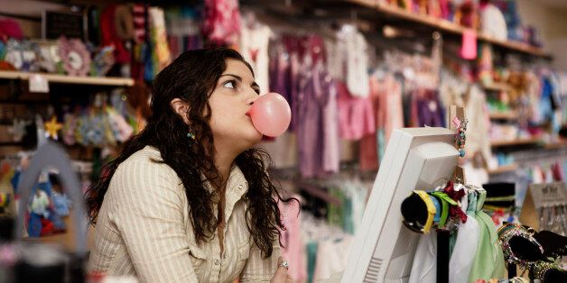 Young woman behind store counter, blowing bubblegum
