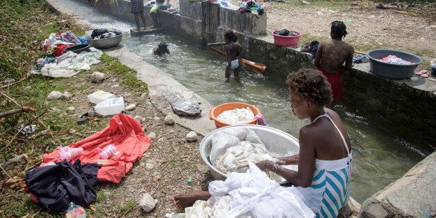 LES CAYES, HAITI - OCTOBER 14: Women wash clothes in a canal while children splash into the water on October 14, 2016 in a small village near Les Cayes, Haiti. After the hurricane clean drinking water is scarce. The people have to be supplied with clean drinking water and the sanitation has to be repaired. Wells and toilets were destroyed by the hurricane Matthew. The water is polluted and there is a great danger that diseases such as cholera can break out. Matthew had heavily devastated the so