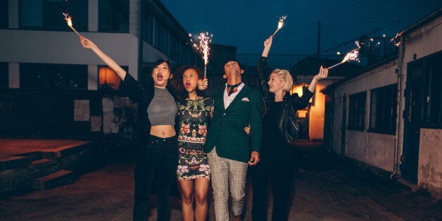 Group of friends enjoying out with sparklers on city street. Young men and women enjoying new years eve on road with fireworks.